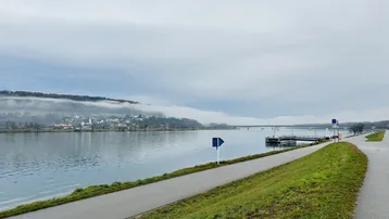 Weitläufiger Blick auf einen Fluss oder See mit einer Brücke und einer Ortschaft am gegenüberliegenden Ufer.