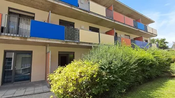 Mehrstöckiges Wohngebäude mit farbigen Balkonbrüstungen und begrünten Außenbereichen.