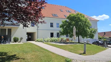Mehrfamilienhaus mit gepflegter Grünfläche, Sitzbereich im Freien und Zugang zum Gebäude.