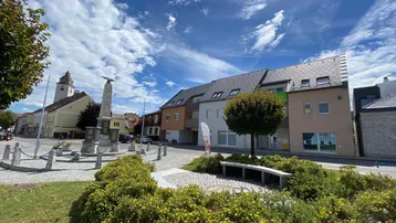 Blick auf die moderne Wohnanlage mit Satteldach und umliegendem Platz bei sonnigem Wetter.
