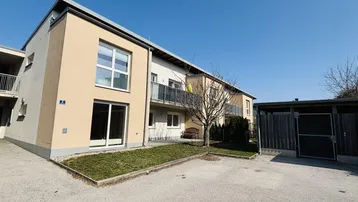 Moderne Wohnanlage mit kleiner Rasenfläche, Gartenhaus und Parkplätzen im Freien.