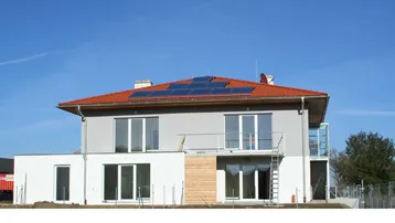 Neubau eines Einfamilienhauses mit rotem Ziegeldach, Photovoltaikanlage und Balkon.