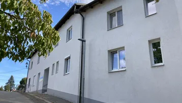 Ansicht der Gebäudefassade mit weißem Putz und mehreren Fenstern unter blauem Himmel.