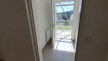 Heller Flur mit Fliesenboden und Zugang zu einem Balkon, der einen weiten Blick ins Grüne bietet.