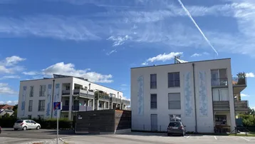 Zwei moderne Mehrfamilienhäuser mit Balkonen und Außenparkplätzen unter blauem Himmel.