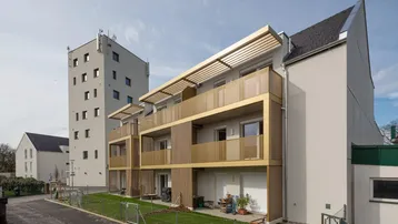 Moderne Wohnanlage mit goldfarbenen Balkonen und privaten Gartenbereichen unter blauem Himmel.