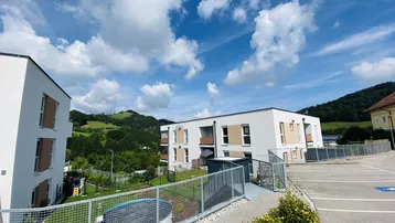 Moderne Wohngebäude mit weißer Fassade und grüner Umgebung unter blauem Himmel.