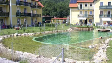 Mehrere gelbe Gebäude mit Balkonen und einem großen Naturschwimmteich in bergiger Umgebung.