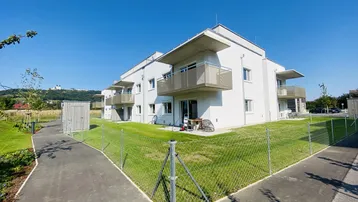 Moderne Wohnanlage mit weißer Fassade, Balkonen und gepflegten Grünflächen unter blauem Himmel.