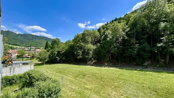 Weitläufiger Blick auf die grüne Landschaft und die bewaldeten Berge unter blauem Himmel.