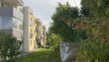 Gemeinschaftlicher Gartenbereich mit Rasenfläche und Sitzgelegenheiten neben dem modernen Wohngebäude.