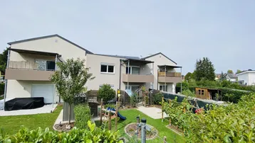 Mehrfamilienhaus mit gepflegtem Garten, Spielplatz und Balkonen im Grünen.