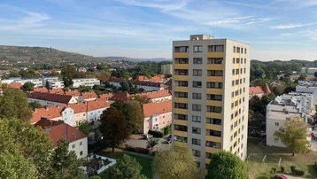 Panoramablick auf das Hochhaus und die umliegende Wohnsiedlung mit Hügeln im Hintergrund.
