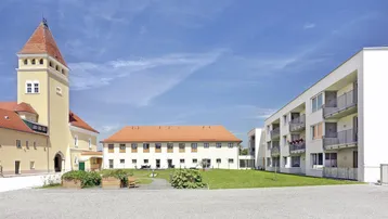 Blick auf einen Gebäudekomplex mit historischem Turm und modernen Wohngebäuden um eine Grünfläche.