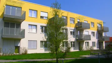 Modernes Mehrfamilienhaus mit gelber Fassade, Balkonen und gepflegter Grünfläche.