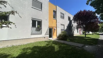 Moderne Wohnhausfassade mit hellem Putz, gelbem Akzent und kleinem französischen Balkon unter blauem Himmel.