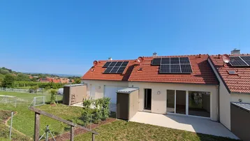 Rückansicht von Reihenhäusern mit Solaranlagen auf den Dächern und privaten Gärten.