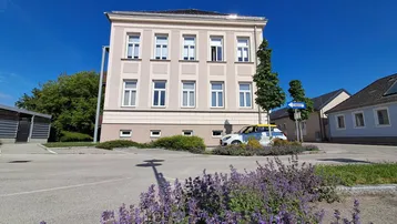 Mehrstöckiges Gebäude mit heller Fassade und weißen Fenstern unter blauem Himmel.