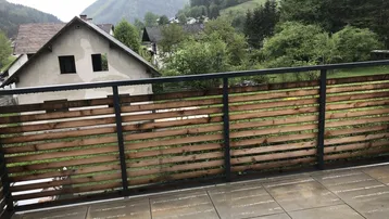Balkon mit Fliesenboden und Holzgeländer, bietet einen weiten Blick auf die bewaldete Umgebung.
