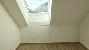 Heller Raum mit Holzfußboden und Dachfenster, das einen malerischen Bergblick bietet.