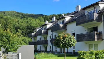 Modernes Mehrfamilienhaus mit Balkonen und Blick auf die grüne Hügellandschaft.