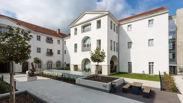 Moderner Innenhof eines weißen Gebäudekomplexes mit Sitzgelegenheiten und Grünflächen.