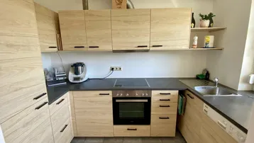 Moderne Küche mit hellen Holzfronten, dunkler Arbeitsplatte, integriertem Backofen und Induktionskochfeld.