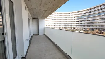 Langer, schmaler Balkon mit Betonboden und weißer Brüstung, bietet Blick auf ein weiteres Gebäude.