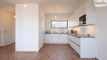 Moderne Einbauküche mit weißen Schränken, Laminatboden und einem Fenster über der Spüle.