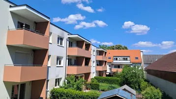 Mehrfamilienhaus mit Balkonen, Gartenbereich und einem kleinen Gartenhaus unter blauem Himmel.