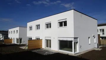 Moderne Reihenhäuser mit weißer Fassade und großen Fenstern in einer Neubausiedlung.