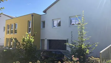Ansicht der modernen Wohnanlage mit gelben Akzenten und umgebender Grünfläche unter blauem Himmel.