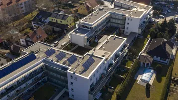 Luftaufnahme einer weitläufigen Wohnanlage mit Flachdächern, Solaranlagen und umliegenden Gärten.