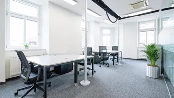 Helles, modernes Büro mit mehreren Arbeitsplätzen, großen Fenstern und Teppichboden für eine angenehme Arbeitsatmosphäre.