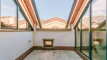 Überdachte Loggia mit Fliesenboden und großen Fenstern, die einen Blick auf die Dächer bieten.