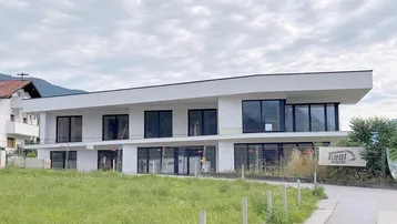 Modernes weißes Gebäude mit großen Fenstern und Blick auf die Berge im Hintergrund.