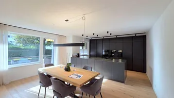 Moderner offener Wohn-Essbereich mit Holzboden, großer Fensterfront und integrierter Küche.