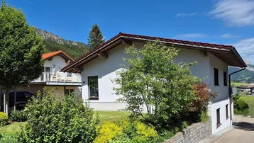 Modernes Einfamilienhaus mit gepflegtem Garten, grüner Umgebung und beeindruckendem Bergblick.
