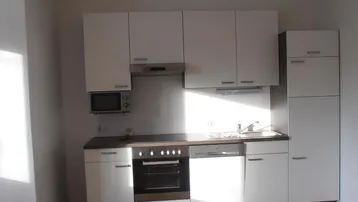 Moderne Einbauküche mit wei ßen Schränken, integrierten Geräten und dunkler Arbeitsplatte.
