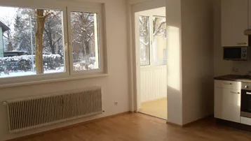 Heller Wohnbereich mit großen Fenstern, Holzboden und Zugang zu einem Balkon.