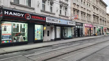 Eine belebte Straße mit Geschäften und Straßenbahnschienen, umgeben von historischen Gebäuden in der Stadt.