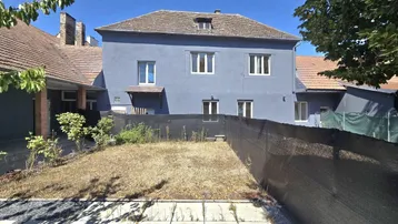 Rückansicht eines blaugrauen Gebäudes mit Gartenbereich und einer schwarzen Sichtschutzwand unter klarem Himmel.