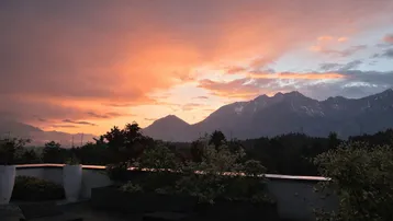 Atemberaubender Sonnenuntergang über den Bergen, genossen von einer stilvollen Dachterrasse mit Lounge-Möbeln und Pflanzen.