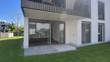 Moderne Wohnanlage mit direktem Gartenzugang und Balkon im Obergeschoss unter strahlendem Sonnenschein.