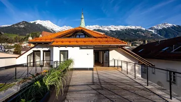 Große Dachterrasse mit Holzboden, Blick auf die Berge und umliegende Gebäude.