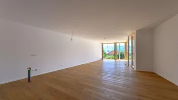 Geräumiges, helles Wohnzimmer mit Holzboden und großen Fenstern, die einen weiten Blick ins Grüne bieten.