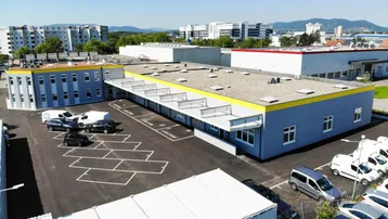 Luftaufnahme eines modernen Gewerbekomplexes mit mehreren Gebäuden und großzügigen Parkflächen unter blauem Himmel.