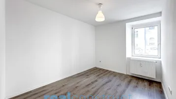 Helles, leeres Zimmer mit Laminatboden und einem Fenster, das viel Tageslicht hereinlässt.