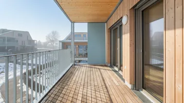 Heller Balkon mit Holzboden und Holzverkleidung, umgeben von winterlicher Landschaft.
