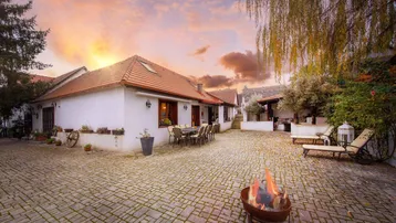 Stimmungsvoller Innenhof bei Sonnenuntergang mit Feuerstelle, Essbereich und Liegestühlen.
